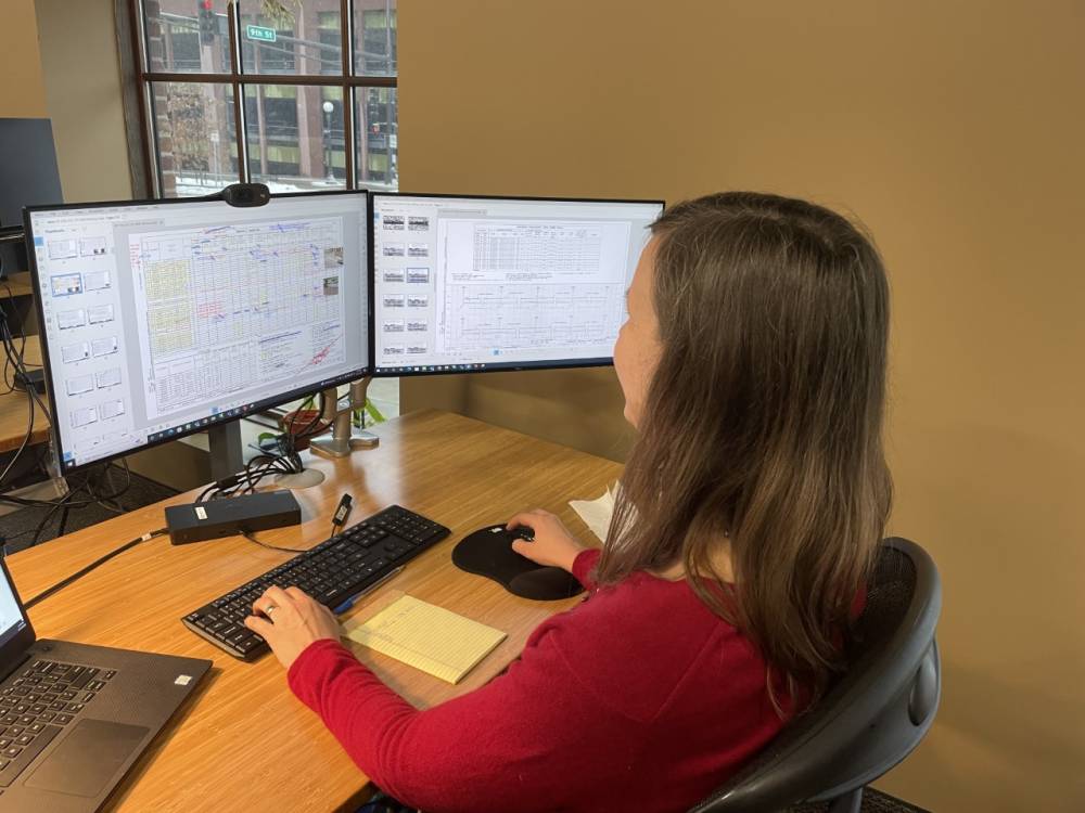 Amy sitting at a desk looking at two computer monitors