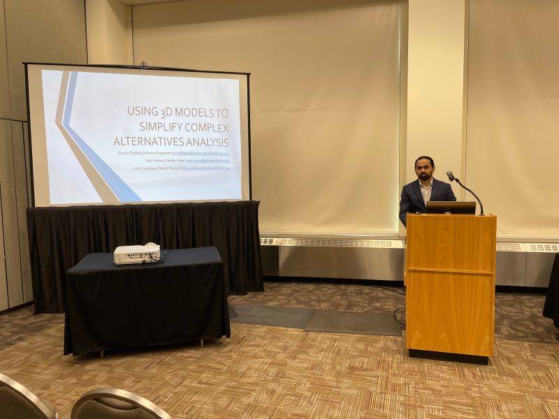 Presentation title slide that says Using 3D Models to Simplify Complex Alternatives Analysis next to Pravin standing behind a podium